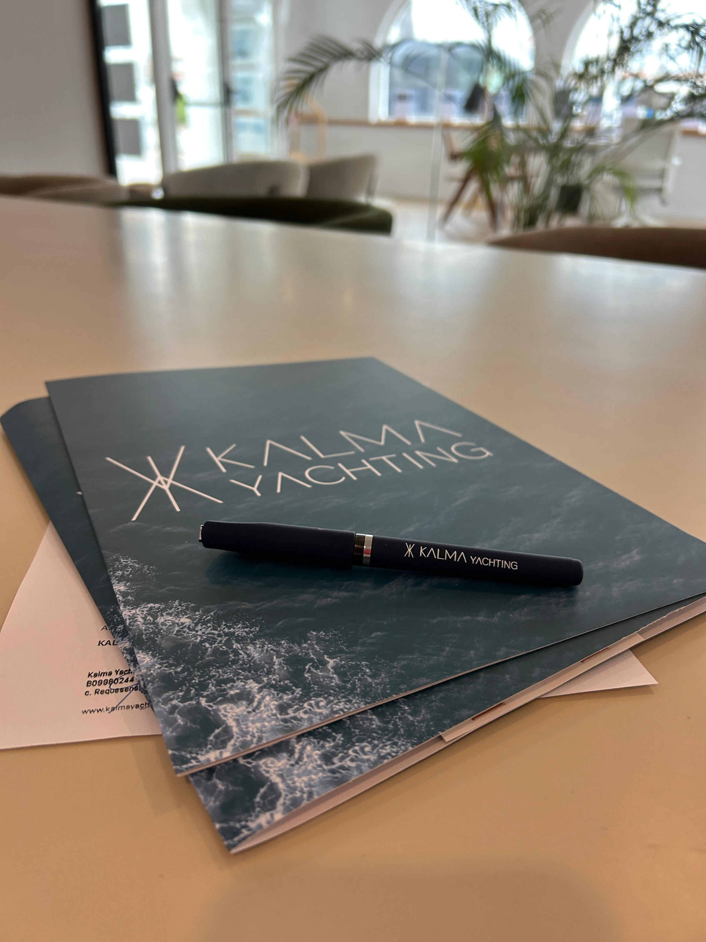 Carpeta y bolígrafo de Kalma Yachting sobre la mesa de reuniones de la oficina